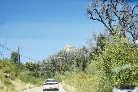 1995 Ford Taurus - A white 1995 Ford Taurus drives down a two-lane road surrounded by dry vegetation and distant mountains under a clear blue sky.