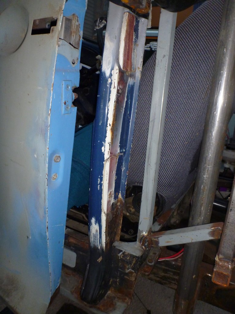 Vehicle interior showing a blue door panel, rusted metal support, and grey patterned upholstery