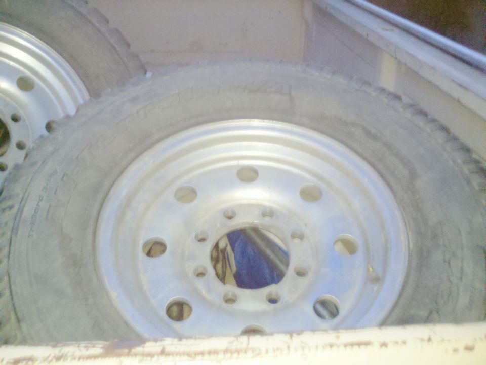 Two truck tires and aluminum wheels stacked in a cargo area. The tires are worn