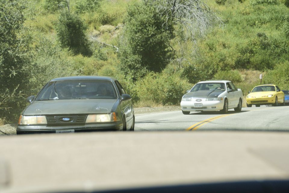 Several cars driving on a road with trees and hills in the background