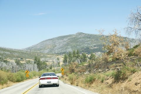 1995 Ford Taurus - A white sedan travels down a two-lane road through a dry, mountainous landscape under a clear blue sky.