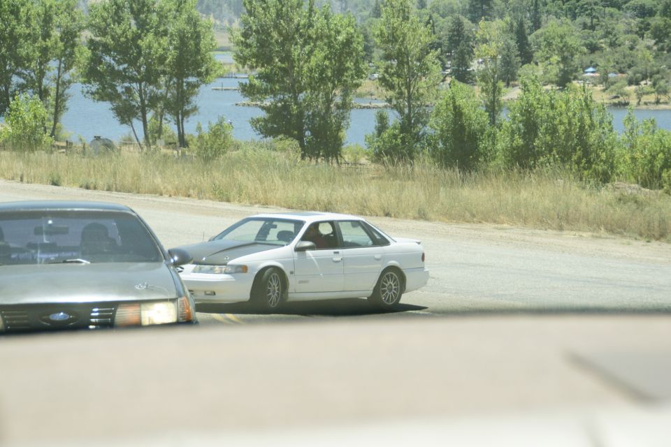 white sedan with black hood driving on a road near a lake