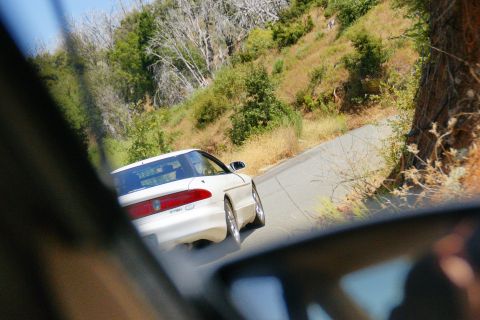 1995 Ford Taurus - A white sedan navigates a rural road, its rear visible in the reflection of a side mirror.