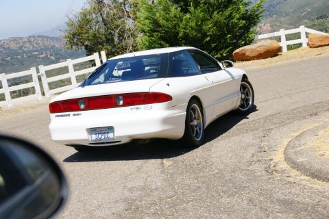 1995 Ford Taurus - This white 1995 Ford Probe is captured from behind as it navigates a scenic, winding road.