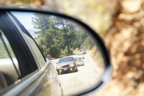 1995 Ford Taurus - A 1995 Ford Taurus is visible in the side mirror, leading a line of vehicles on a rural road.
