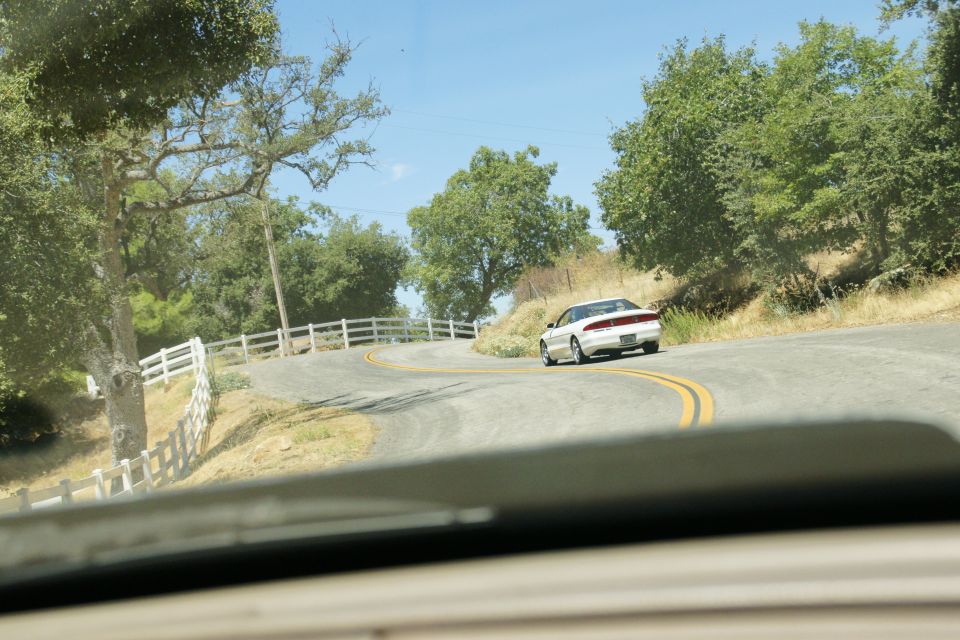 White 1995 Ford Taurus sedan driving on a winding road, rear view