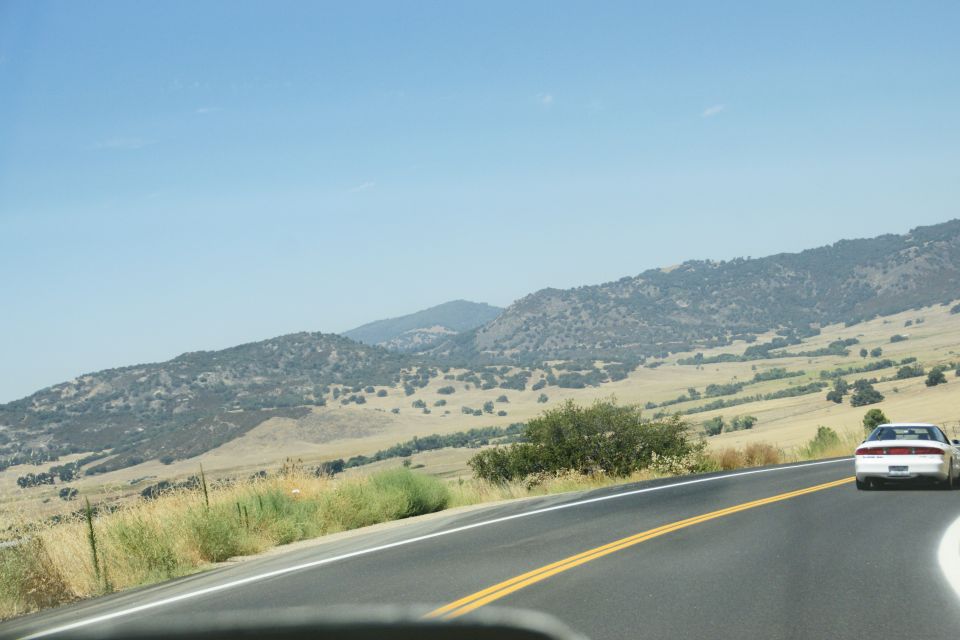 White sedan driving on a highway with rolling hills and blue sky