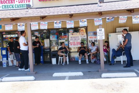 1995 Ford Taurus - People gather outside a convenience store on a sunny day, with various signs and advertisements displayed.