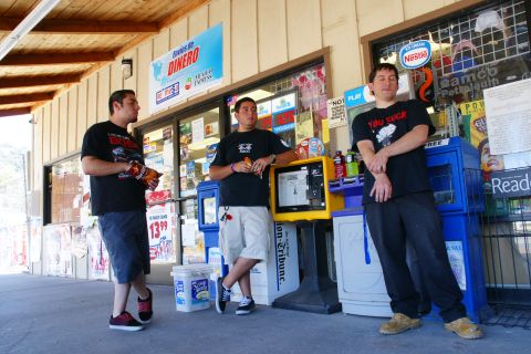 1995 Ford Taurus - Three men are gathered outside a store entrance, with one man holding a bag of chips and another leaning on a kiosk.