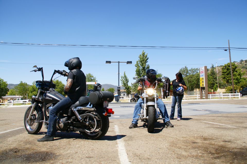 Two people on motorcycles, one person standing nearby. Sunny day