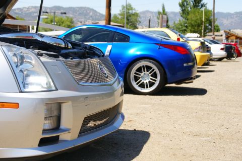 1995 Ford Taurus - A row of cars, including a silver Cadillac and a blue sports car, are parked outdoors on a sunny day.