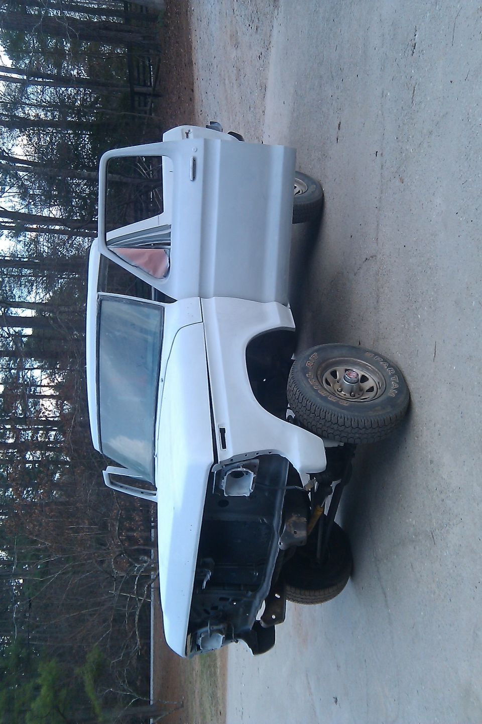 White 1978 Ford Bronco body, primer gray, with doors open, front end removed, parked outdoors