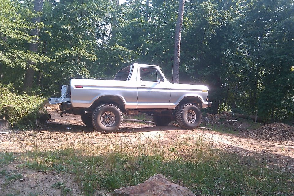 Silver 1978 Ford Bronco parked on a dirt path with trees in the background