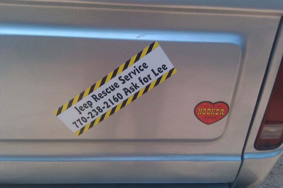 Silver vehicle rear panel with 'Jeep Rescue Service 770-238-2160 Ask for Lee' sticker and a red heart sticker that says 'HOOKER'