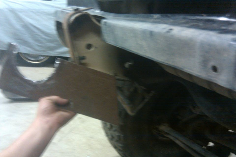 hand holding a metal bracket against a vehicle frame, possibly for repair