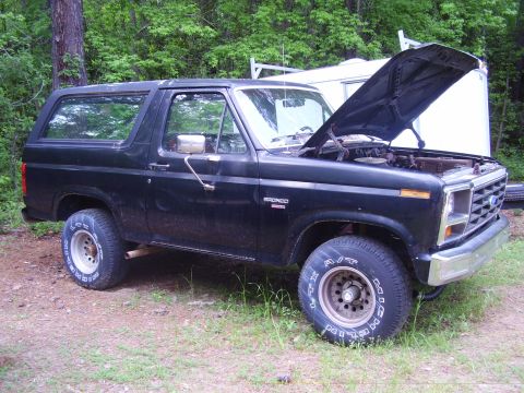 1986 Ford Bronco - Black 1986 Ford Bronco with hood open, parked on a dirt and grass area.