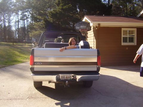 1988 Ford Bronco - A person leans over the tailgate of a 1988 Ford Bronco, parked in a driveway.
