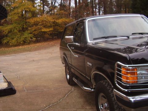 1988 Ford Bronco - A black SUV is parked on a concrete driveway with autumn trees in the background.