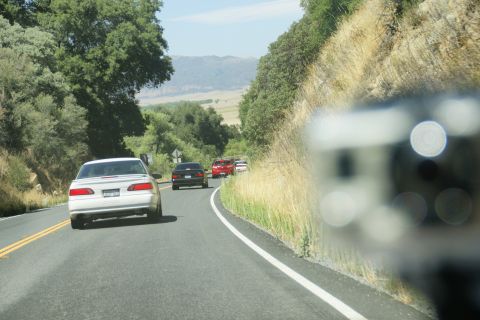 1995 Ford Taurus - Multiple vehicles travel along a scenic, winding road with grassy hillsides.