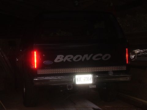 1986 Ford Bronco - The rear of a black Ford Bronco is shown with its taillights illuminated and a license plate.