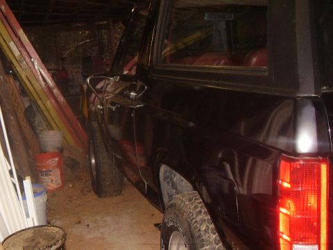 1986 Ford Bronco - Side view of a dark 1986 Ford Bronco parked indoors, showing its red interior.