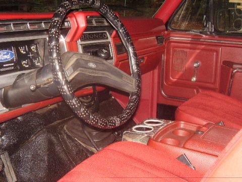 1986 Ford Bronco - The interior of a classic Ford Bronco features red upholstery and a dashboard with the Bronco nameplate.