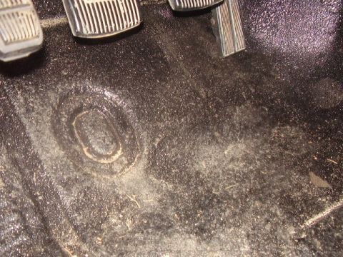 1986 Ford Bronco - Close-up of the interior floor mat and pedals, showing wear and a circular imprint.