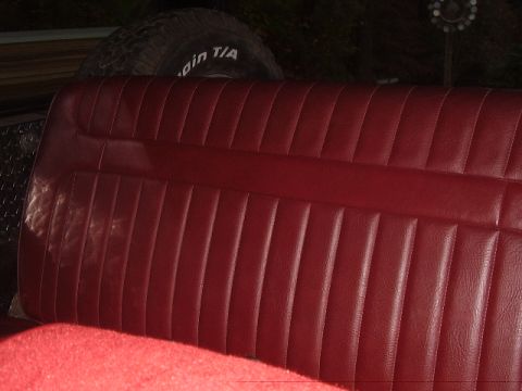 1986 Ford Bronco - Interior view of a red vinyl bench seat with a spare tire in the background.