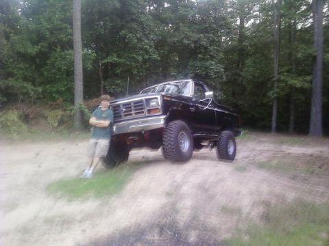 1986 Ford Bronco - A person stands next to a lifted black Ford Bronco in a wooded area.