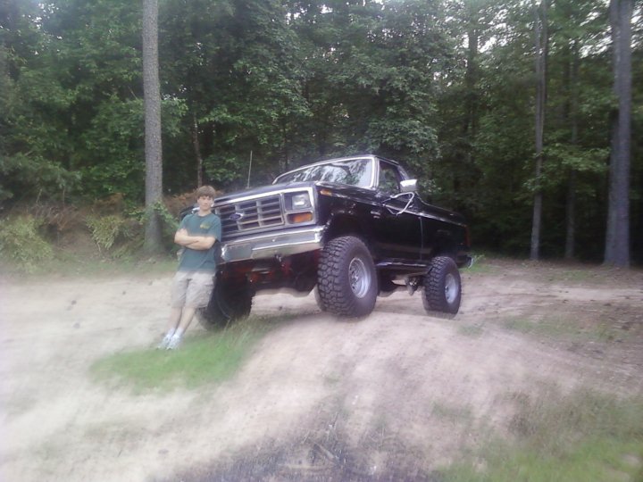 Black Ford Bronco with large tires, lifted suspension, and a person leaning on the front fender