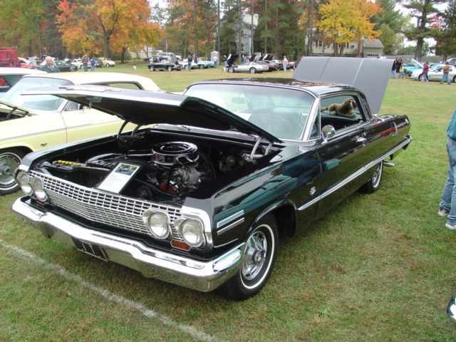 Black 1963 Chevrolet Impala SS hardtop with hood up showing engine, parked on grass at fall car show