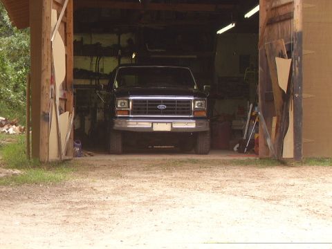 1986 Ford Bronco - A dark-colored Ford truck is parked inside an open-sided garage.