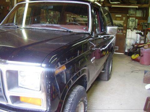 1986 Ford Bronco - This black Ford Bronco is parked in a garage, showing its front 3/4 view with visible chrome trim.