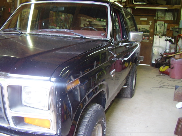 Black Ford Bronco, front 3/4 view, in a garage. Chrome trim and side mirror visible