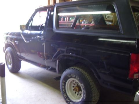 1986 Ford Bronco - The side profile of a dark-colored Ford Bronco is visible, showing its wheels and windows.