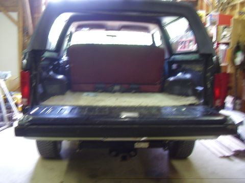 1986 Ford Bronco - The rear of a dark-colored SUV is shown with its tailgate open, revealing the interior and red seats.
