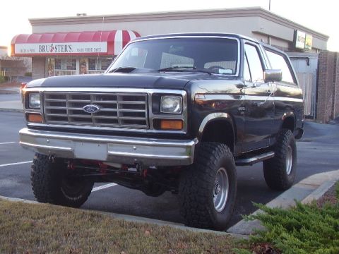 1986 Ford Bronco - This lifted Ford Bronco is parked in front of a building with a red and white awning.