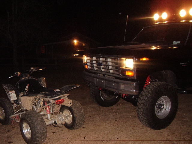 Black pickup truck with off-road tires and lights next to a muddy ATV