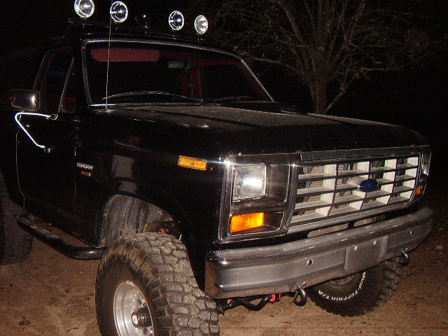 Black 1986 Ford Bronco front 3/4 view with off-road tires and roof lights