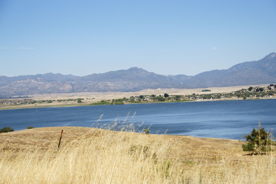 Dry grass in foreground with a blue lake and mountains in the background under a clear sky