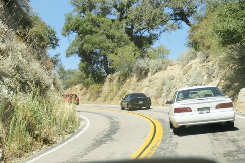 1995 Ford Taurus - Multiple vehicles navigate a scenic, winding road through a dry, hilly landscape.