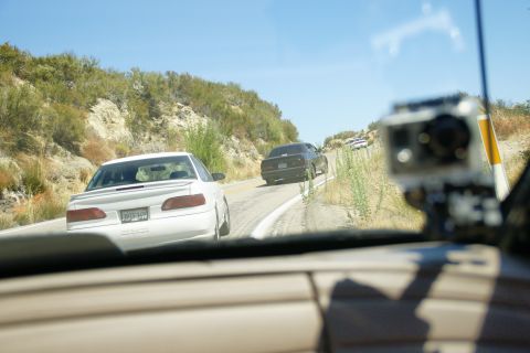 1995 Ford Taurus - A white 1995 Ford Taurus sedan is seen from inside a vehicle, driving on a sunny, winding road with other cars ahead.