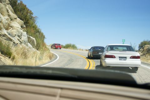 1995 Ford Taurus - A white 1995 Ford Taurus is seen from behind on a mountain highway, with two other vehicles ahead.
