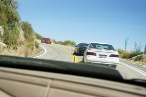 1995 Ford Taurus - Multiple vehicles navigate a scenic mountain highway on a sunny day.