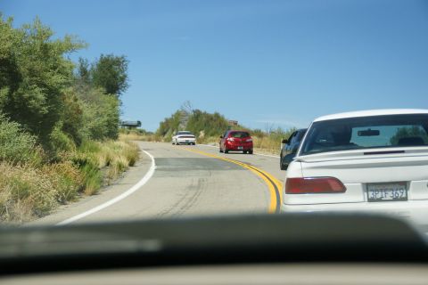 1995 Ford Taurus - Several cars travel along a scenic, curving road under a clear blue sky.