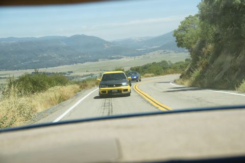 1995 Ford Taurus - Two cars travel along a scenic, winding mountain road under a clear blue sky.