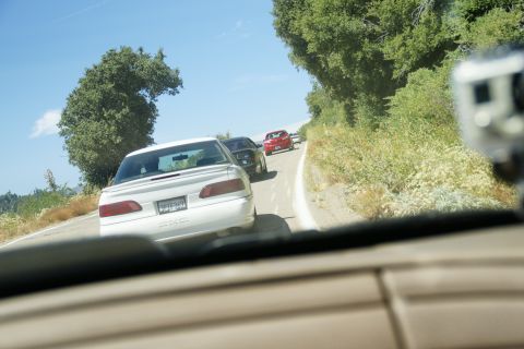 1995 Ford Taurus - A white sedan is seen from behind, driving on a road with other vehicles and trees lining the sides.