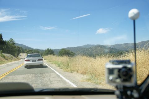 1995 Ford Taurus - A white sedan drives down a rural highway under a clear blue sky with scattered clouds.