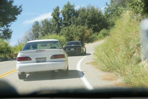 1995 Ford Taurus - Two cars drive on a winding road through a wooded area on a sunny day.