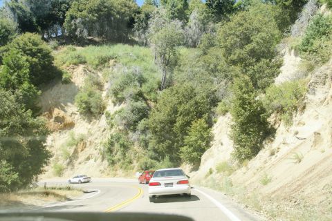 1995 Ford Taurus - Cars navigate a scenic mountain road with steep, vegetated slopes.